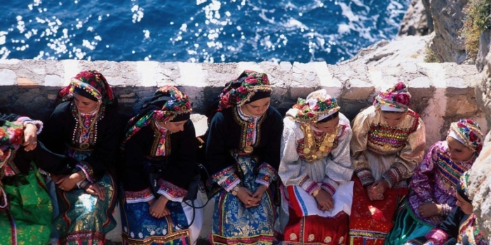 Karpathos, Olymbos: Untouched by Time Vroukounda, young girls in traditional  costumes sit on a stone parapet